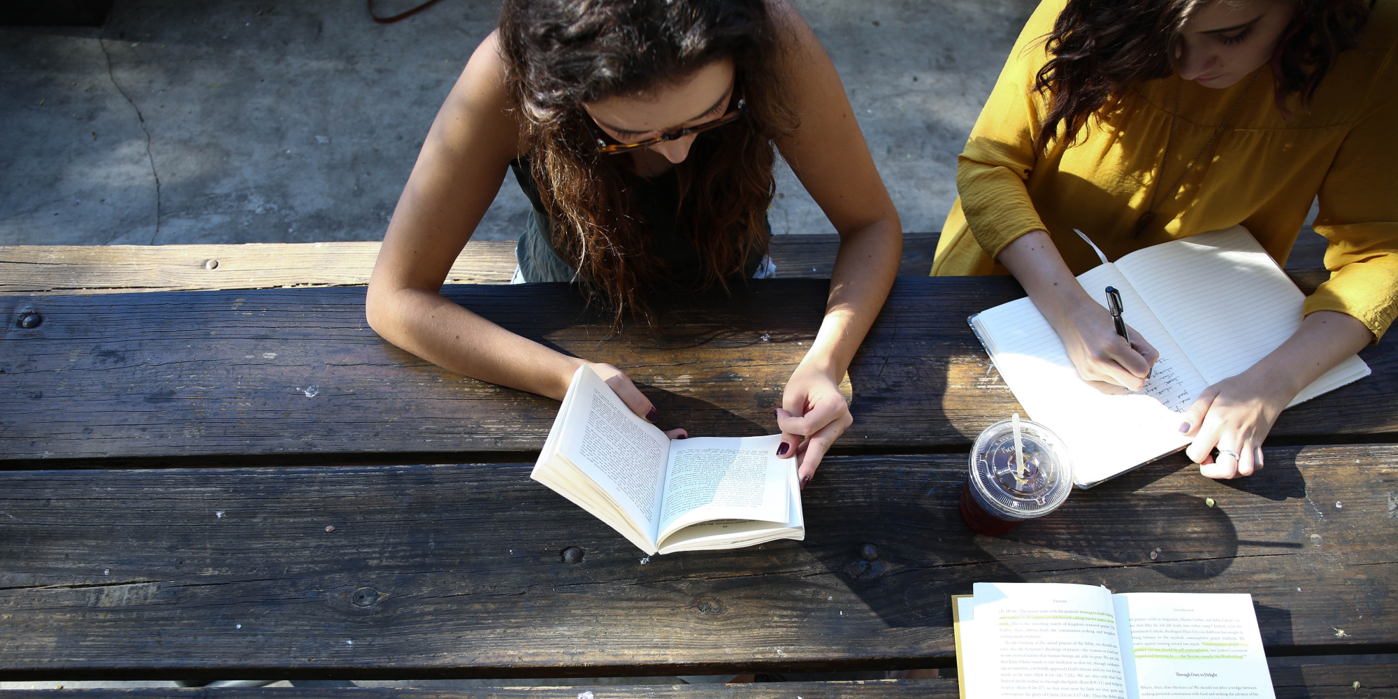 Kaksi nuorta naista istuu ulkona pöydäm ääressä lukemassa ja kirjoittamassa.