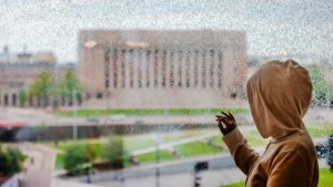 Ruskea nuori katsoo eduskuntataloa lasin läpi