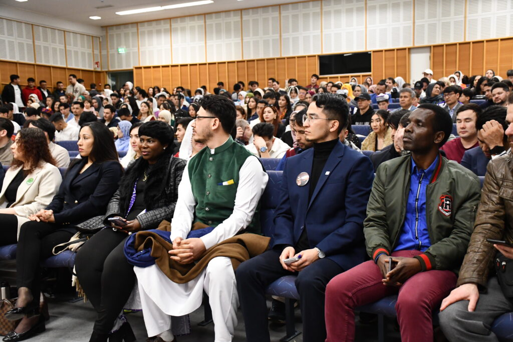 Suuri joukko eri taustaisia ihmisiä istuu katsomossa