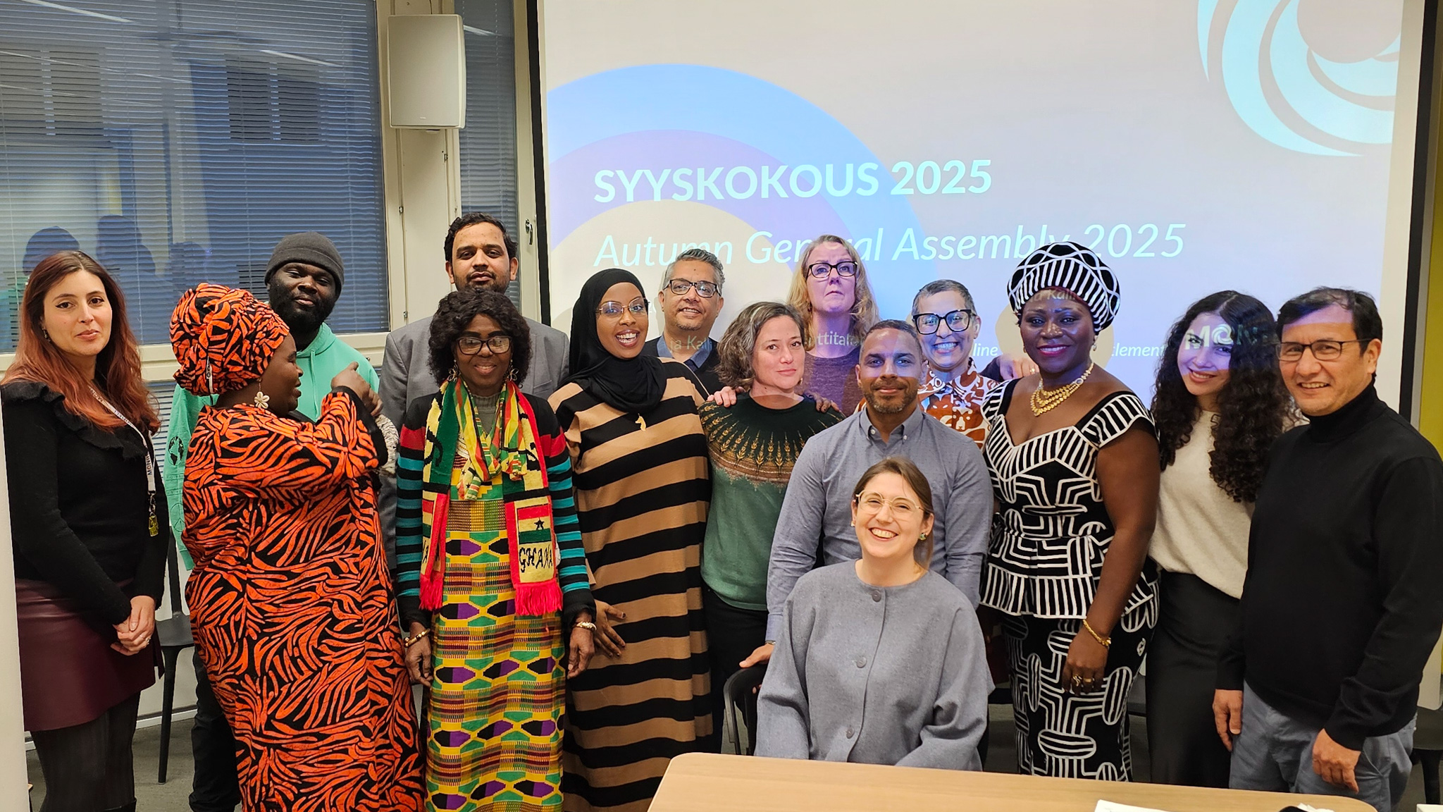 Monihelin syyskokouksen osallistujat. Kuvassa 15 henkilöä juhlavaatteissa, Monihelin toiminnanjohtaja Julie Breton istuu edessä.