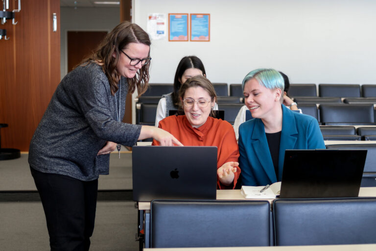 Nainen osoittaa jotakin tietokoneen näytöltä. Kaksi muuta naista katselee vieressä.